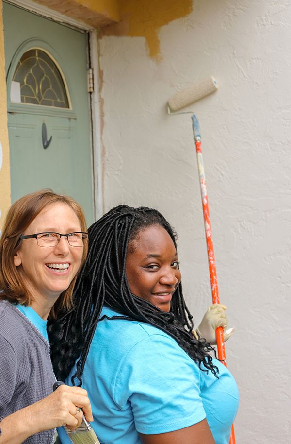 Two young women using roller brush to paint house