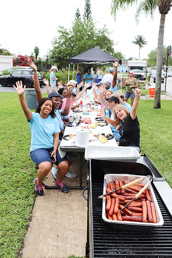NET volunteers sitting at a picnic table on a residential sidewalk, having lunch and waiving at came